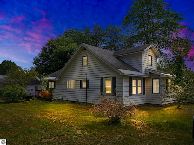 back house at dusk featuring a lawn