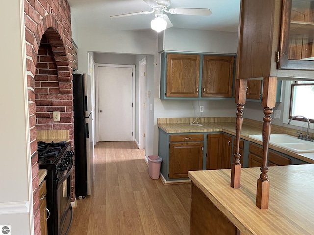 kitchen with ceiling fan, black gas stove, light wood-type flooring, refrigerator, and sink