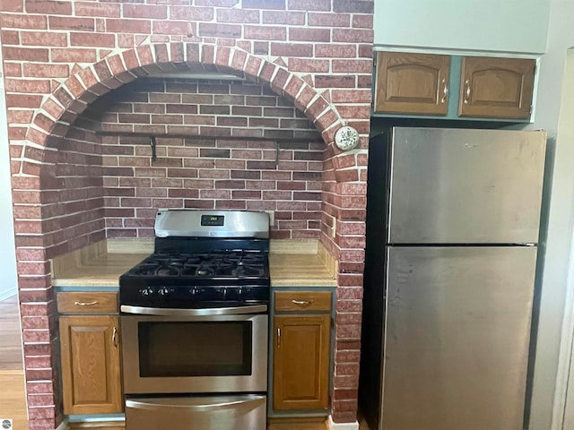 kitchen featuring hardwood / wood-style floors, stainless steel appliances, and brick wall