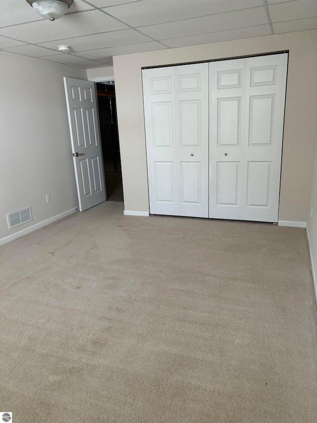 unfurnished bedroom featuring a paneled ceiling, light carpet, and a closet