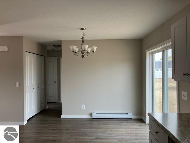 unfurnished dining area with a baseboard radiator, an inviting chandelier, and dark hardwood / wood-style flooring