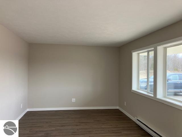 spare room featuring a baseboard heating unit and dark wood-type flooring