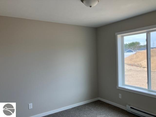 spare room with a baseboard heating unit, a wealth of natural light, and carpet floors