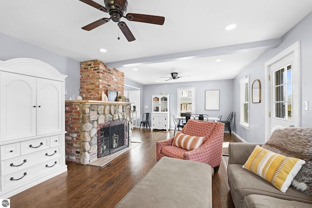 living room featuring dark wood-type flooring, ceiling fan, beamed ceiling, and a fireplace