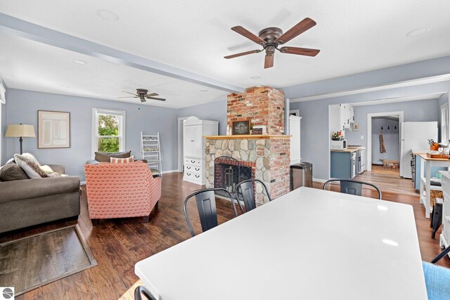 dining area with ceiling fan, dark hardwood / wood-style flooring, beamed ceiling, and a brick fireplace