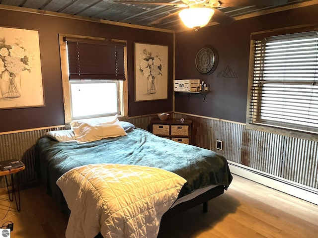 bedroom featuring wooden ceiling, wooden walls, wood finished floors, baseboard heating, and wainscoting