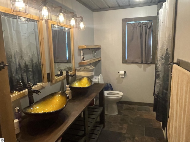 full bathroom featuring toilet, a sink, baseboards, double vanity, and stone finish flooring