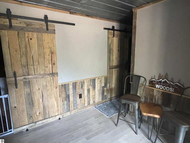 interior space with a wainscoted wall, a barn door, wooden walls, and wood finished floors