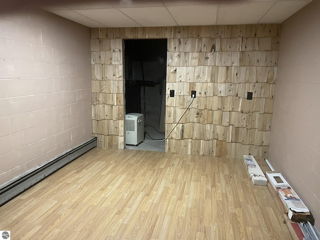 interior space featuring baseboard heating, a drop ceiling, wood finished floors, and concrete block wall