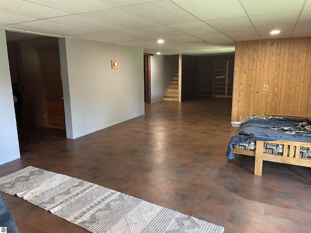 unfurnished bedroom with concrete flooring, concrete block wall, and a paneled ceiling