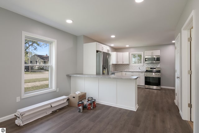 kitchen with dark wood-type flooring, kitchen peninsula, appliances with stainless steel finishes, and white cabinets