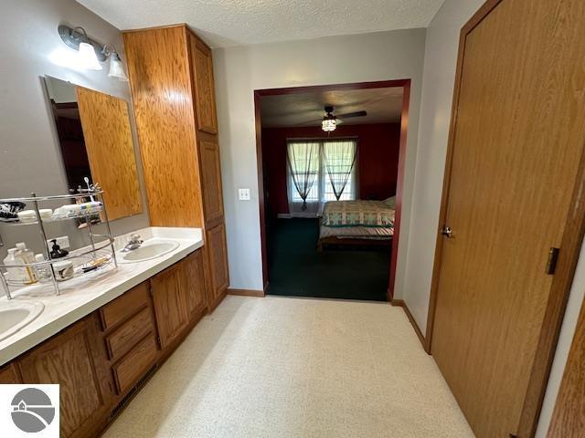 ensuite bathroom featuring baseboards, double vanity, a sink, a textured ceiling, and connected bathroom