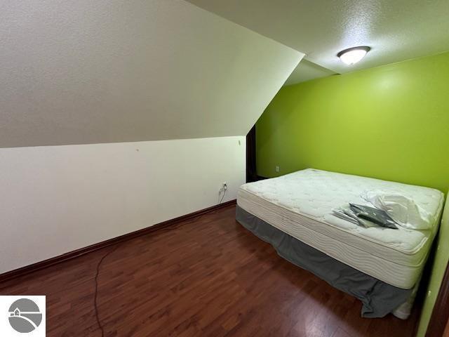 unfurnished bedroom with a textured ceiling, vaulted ceiling, and dark hardwood / wood-style flooring