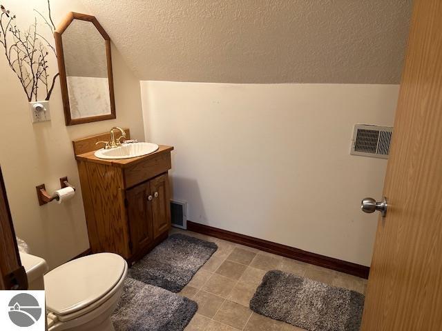 bathroom with vanity, toilet, a textured ceiling, and lofted ceiling