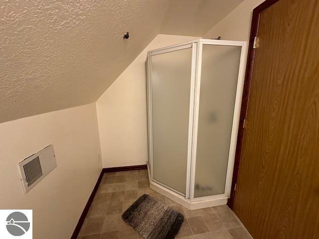 bathroom featuring visible vents, a stall shower, a textured ceiling, and vaulted ceiling