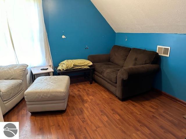 living room with vaulted ceiling, baseboards, visible vents, and wood finished floors