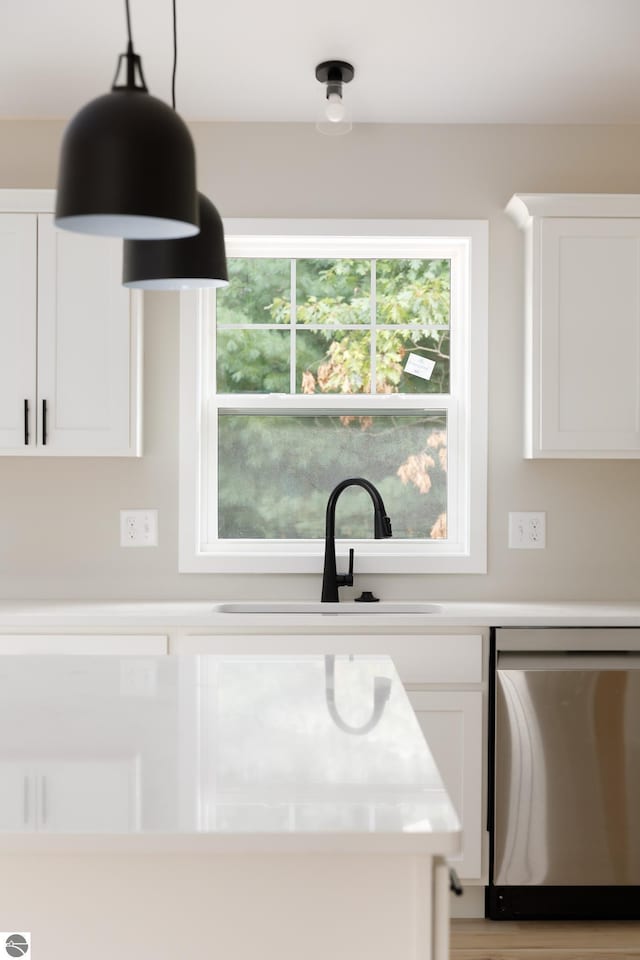 kitchen with light countertops, dishwasher, a sink, and white cabinetry