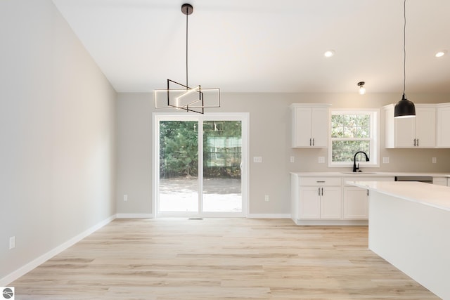 kitchen featuring light countertops, white cabinetry, a sink, light wood-type flooring, and baseboards