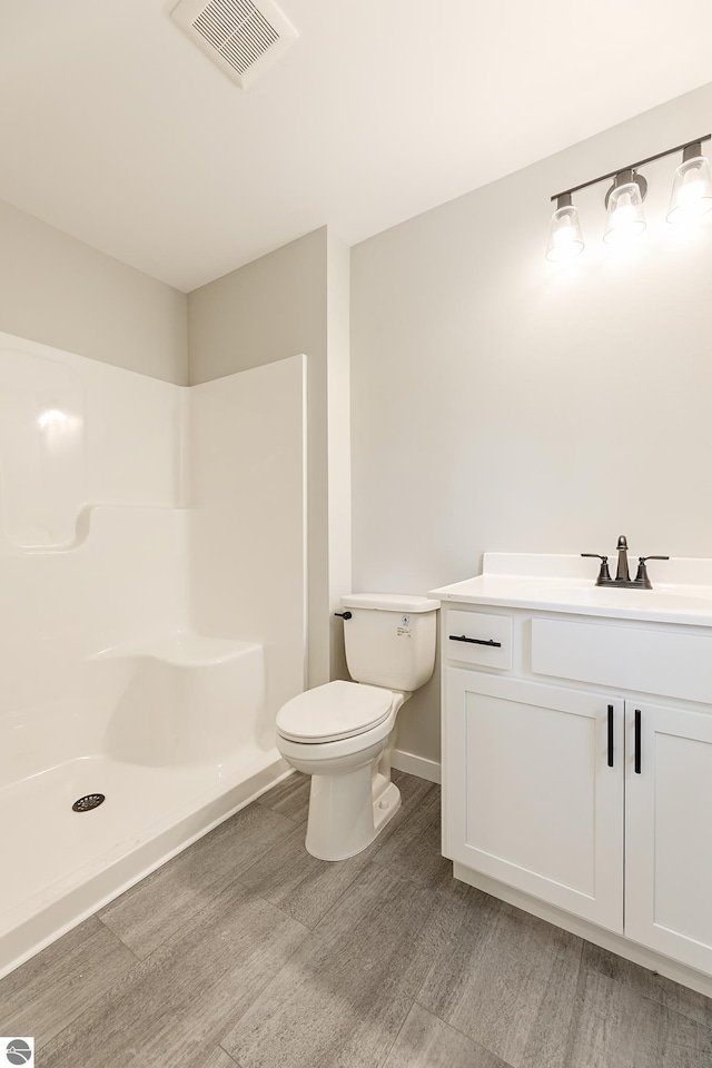 bathroom with visible vents, toilet, vanity, wood finished floors, and walk in shower