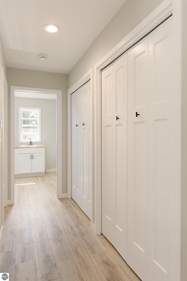 corridor with light wood finished floors, baseboards, and a sink