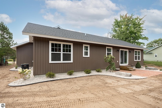 rear view of house featuring central AC unit and roof with shingles