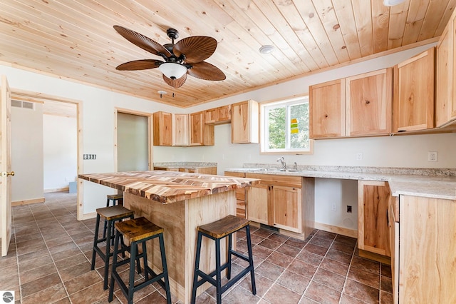 kitchen featuring light brown cabinetry, a center island, a kitchen breakfast bar, ceiling fan, and butcher block counters