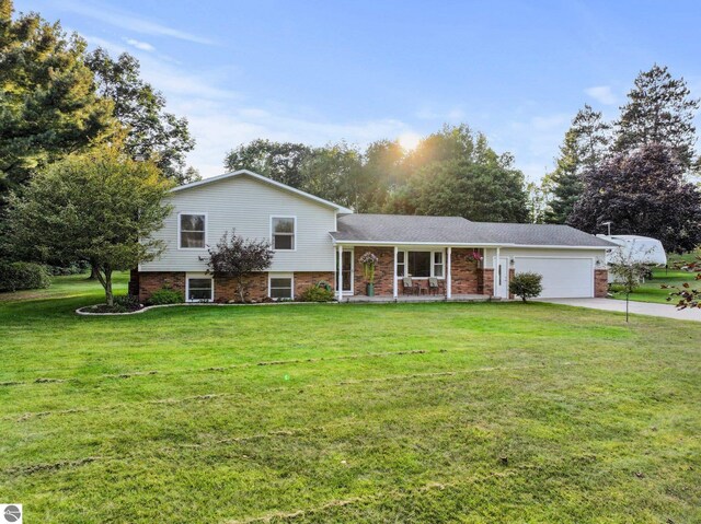 9090 Windsong Ln, Cadillac, MI 49601 - split level home with driveway, a porch, a garage, brick siding, and a front lawn