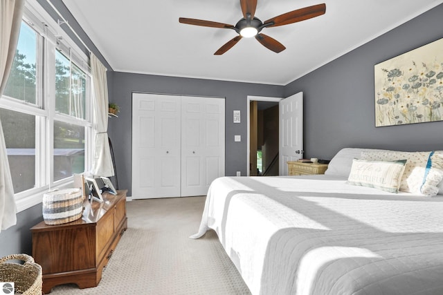 bedroom with ornamental molding, ceiling fan, light colored carpet, and a closet