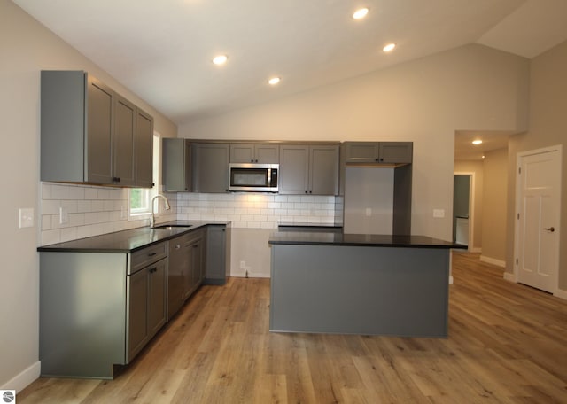 kitchen featuring lofted ceiling, sink, gray cabinetry, a kitchen island, and light wood-type flooring