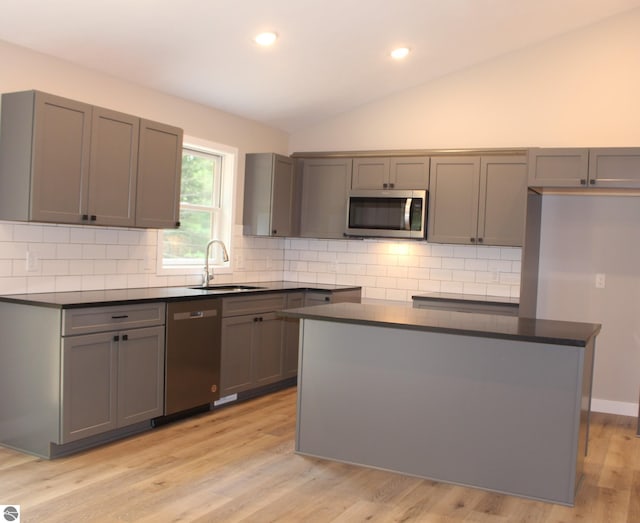 kitchen with lofted ceiling, sink, gray cabinetry, appliances with stainless steel finishes, and a kitchen island