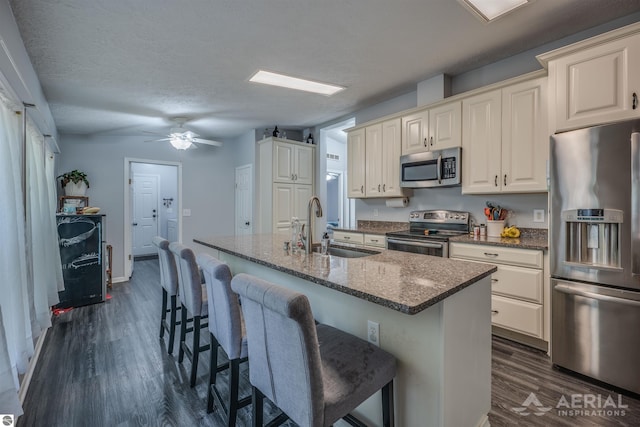 kitchen featuring stainless steel appliances, dark hardwood / wood-style flooring, sink, ceiling fan, and a kitchen island with sink