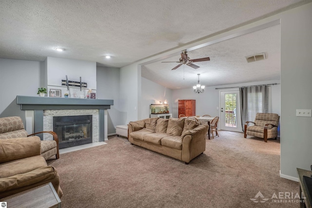 carpeted living room featuring ceiling fan with notable chandelier, vaulted ceiling, a textured ceiling, and a stone fireplace