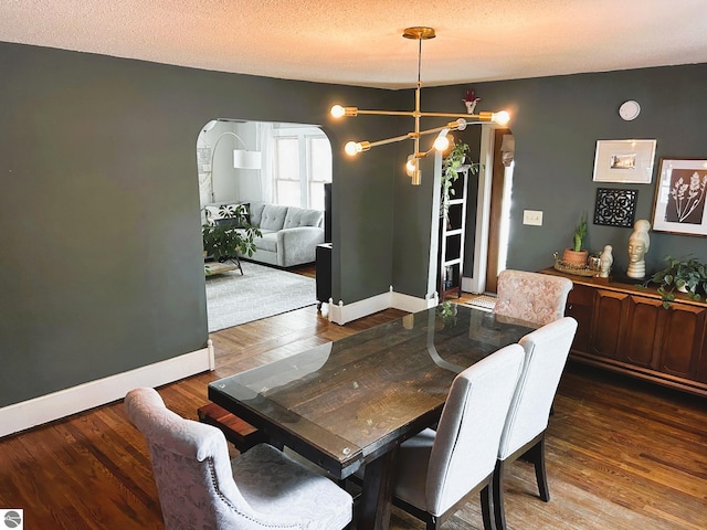 dining space with a textured ceiling, dark wood-type flooring, and an inviting chandelier