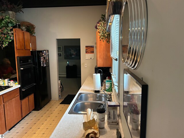 kitchen featuring stovetop, baseboard heating, sink, and black fridge