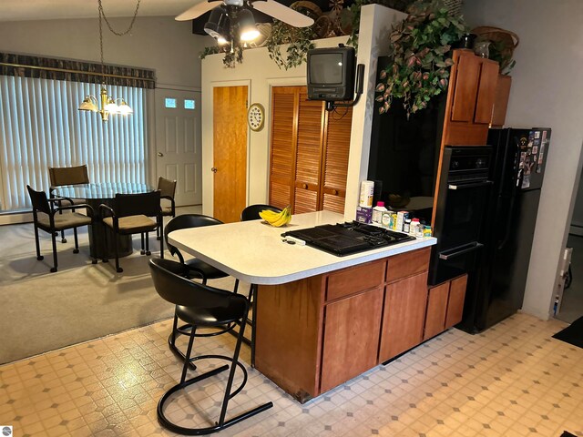 kitchen featuring ceiling fan with notable chandelier, a kitchen bar, decorative light fixtures, black gas stovetop, and vaulted ceiling