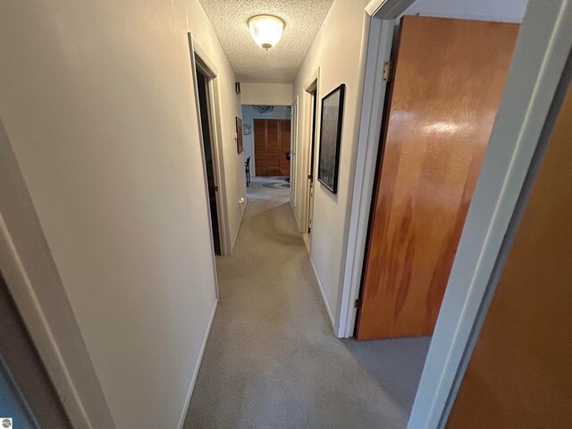 corridor featuring a textured ceiling and light colored carpet