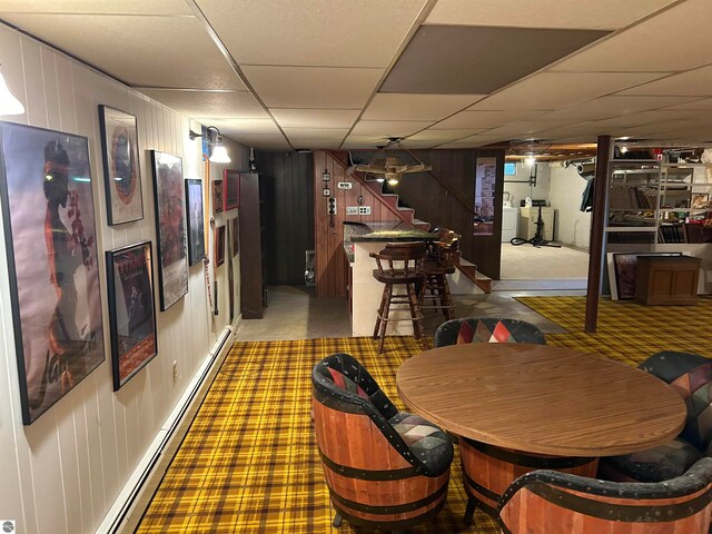 dining room featuring washer / dryer, a paneled ceiling, a baseboard radiator, and wooden walls