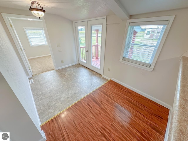 entryway with light wood-type flooring, french doors, a textured ceiling, and lofted ceiling