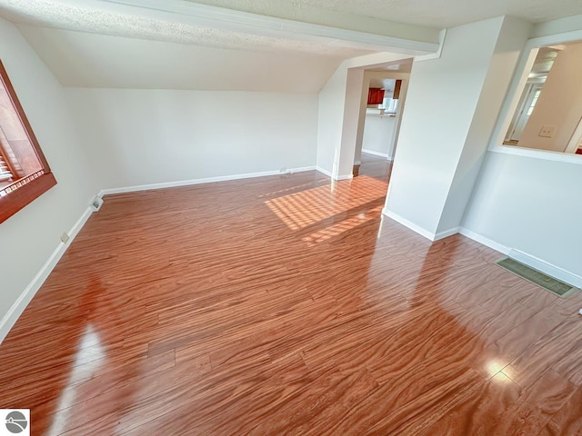 spare room featuring vaulted ceiling, a textured ceiling, and wood-type flooring