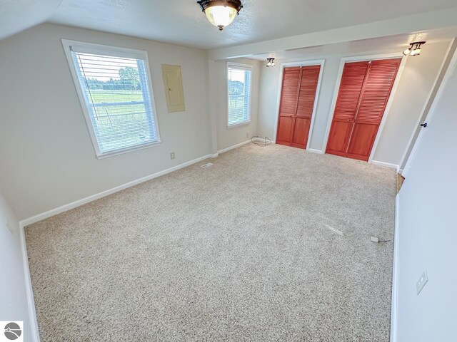 unfurnished bedroom featuring multiple windows, vaulted ceiling, two closets, and carpet