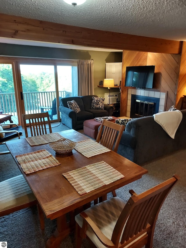 carpeted dining room featuring a textured ceiling, plenty of natural light, a tiled fireplace, and wooden walls