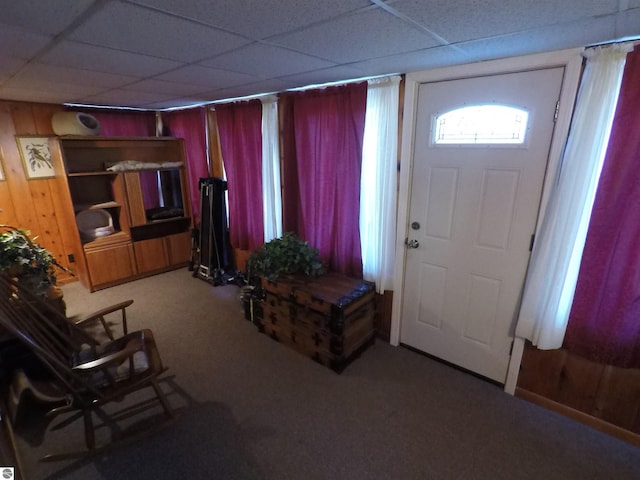 foyer featuring wood walls, a drop ceiling, and carpet floors