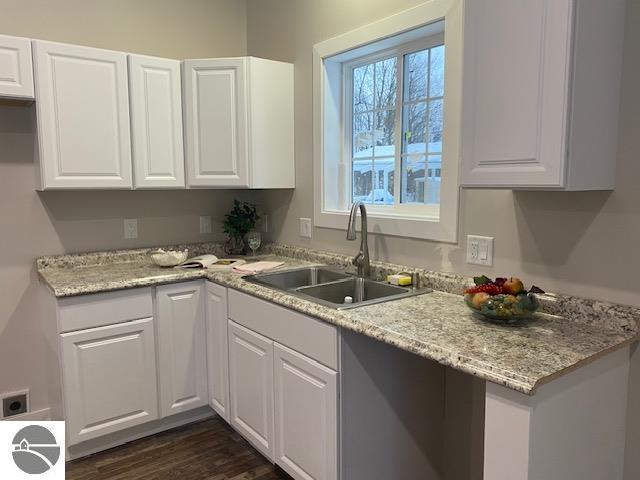 kitchen with light stone counters, sink, white cabinets, and dark hardwood / wood-style floors