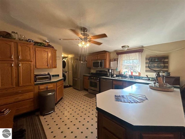 kitchen featuring stainless steel appliances, ceiling fan, stacked washer / drying machine, and a textured ceiling