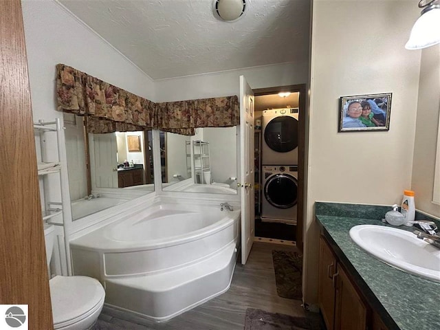 bathroom with a bathing tub, hardwood / wood-style flooring, lofted ceiling, stacked washing maching and dryer, and toilet