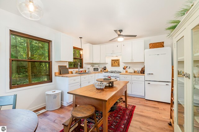 kitchen with white cabinets, white appliances, light hardwood / wood-style flooring, decorative light fixtures, and sink