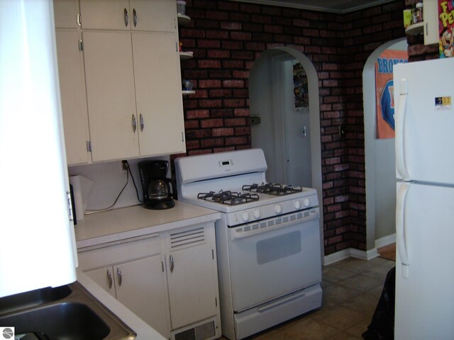 413 N Fancher St, Mount Pleasant, MI 48858 - kitchen with white appliances, brick wall, arched walkways, light countertops, and white cabinetry