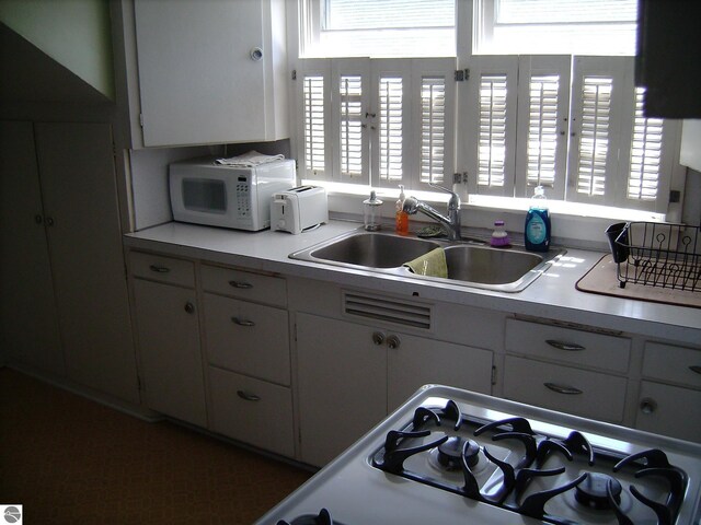 413 N Fancher St, Mount Pleasant, MI 48858 - kitchen featuring white microwave, light countertops, stovetop, white cabinetry, and a sink