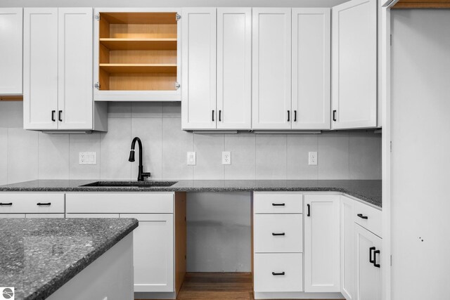 kitchen with sink, white cabinetry, decorative backsplash, hardwood / wood-style floors, and dark stone countertops