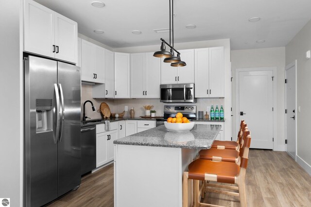 kitchen with decorative light fixtures, stainless steel appliances, light hardwood / wood-style floors, and a kitchen island